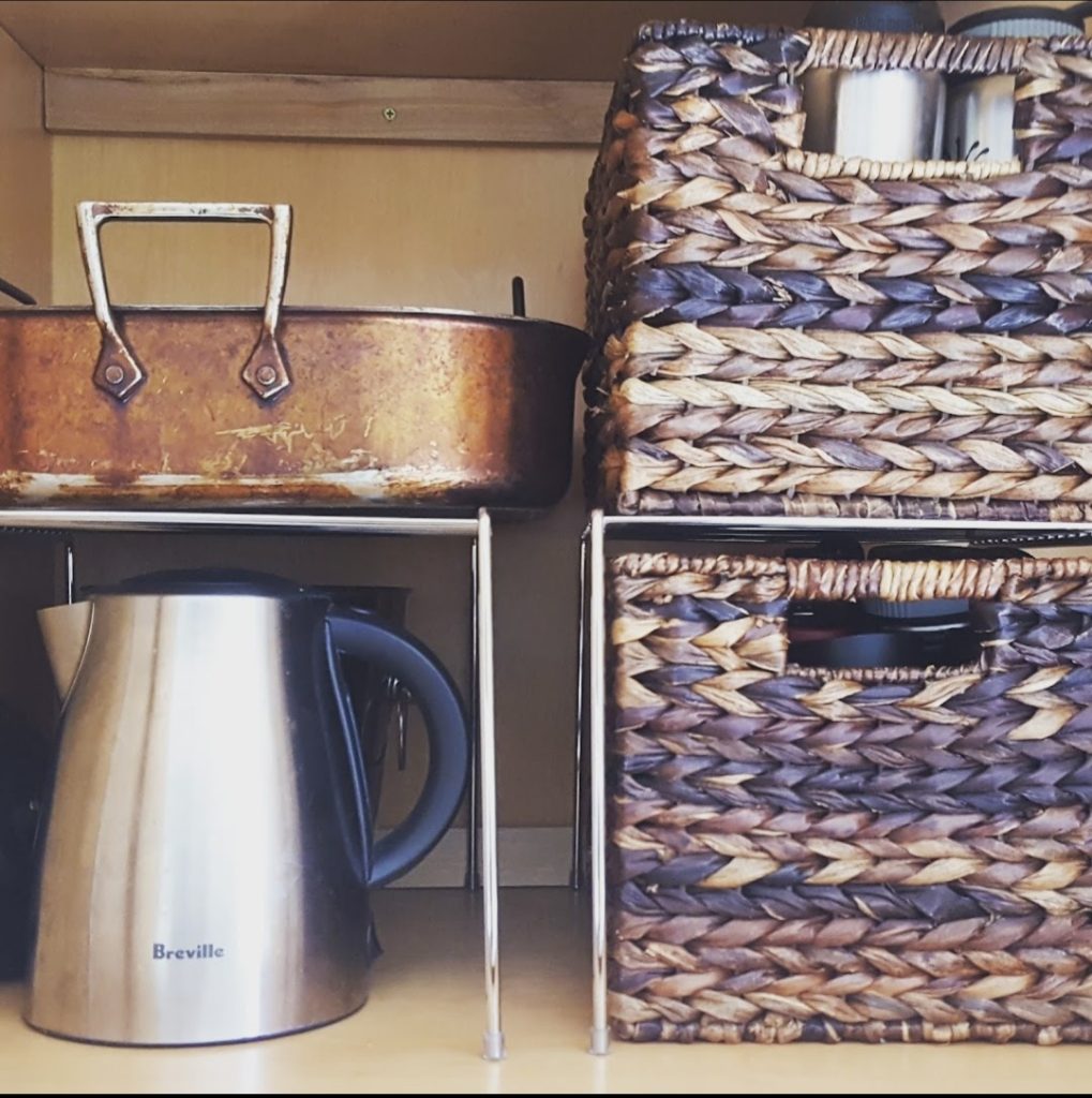 kitchen unpack and organize into cabinet with space saver metal shelf riser and brown natural weave baskets from container store stainless steel water tea kettle Bella Organizing Professional home organizers and residential packing and moving management company serving the San Francisco Bay Area.